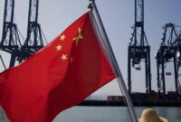 1765105585160-sebuah-bendera-china-yang-sedang-berkibar-di-depan-mesin-pengangkut-kargo-di-pelabuhan-di-china_169